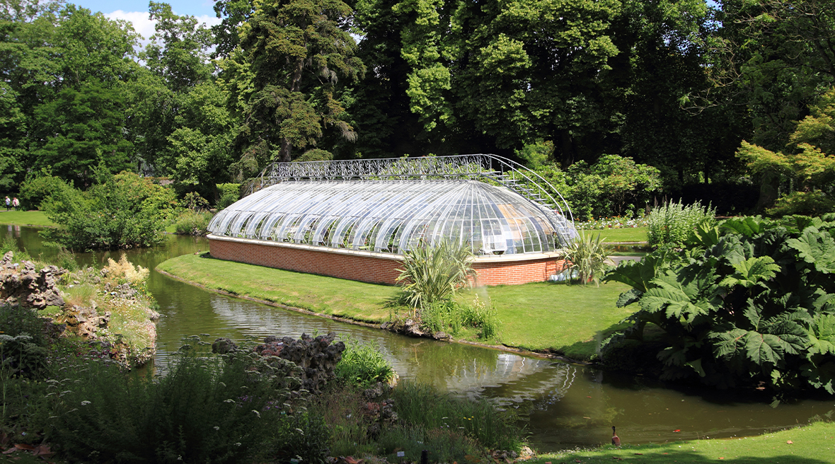 large greenhouse building set amongst parkland and big green trees on a sunny day
